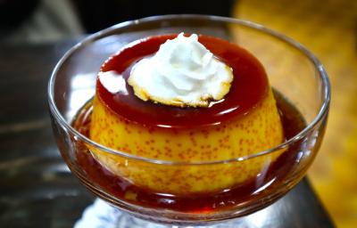 Fotografia de um mini pudim de café dentro de uma taça pequena de vidro com a calda de caramelo. Por cima do pudim tem um pouco de chantilly.