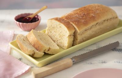 Receita de Pão de Leite Moça. Observa-se um pão cortado com três fatias sob uma forma retangular verde clara. Ao lado, uma faca de pão e do outro, um potinho com geleia.