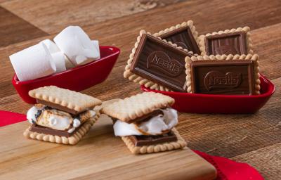 Fotografia em tons de vermelho com vários recipientes vermelhos ao centro. Dentro de um dos recipientes, existe dois biscoitos Choco Biscuit recheados com marsmallow. Ao lado existe marshmallows e biscoitos Choco Biscuit NESTLÉ