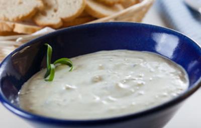 Fotografia em tons de branco e azul, ao centro recipiente de porcelana azul com patê de Gorgonzola, cestinha com torradas ao fundo e ao lado um guardanapo azul claro com listras em azul escuro.