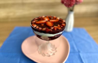 Fotografia em tons de rosa e azul com uma taça de vidro ao centro. Em cima da taça existe uma receita de açaí com frutas e ASCENDA