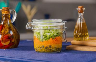 Fotografia em tons de azul com um pote de vidro ao centro. Dentro do pote existe uma receita de salada com molho de maracujá, cenoura e acelga