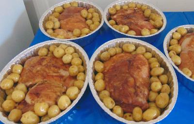 Foto da receita de Pernil Assado com Batatas Coradas. Observa-se 5 travessas de alumínio com o pernil dentro bem dourado e muitas batatinhas ao redor.