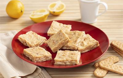 Fotografia em tons de amarelo, vermelho e branco de um paninho listrado amarelo e branco, sobre ele um prato redondo vermelho com palha italiana. Ao lado um paninho branco e biscoitos tostines maizena. Ao fundo uma xícara branca e dois limões.