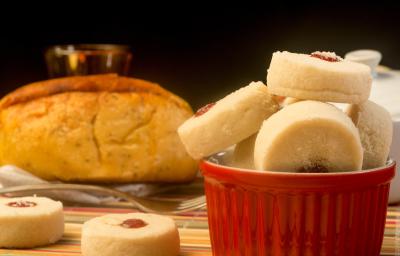 Fotografia de biscoitinhos amanteigados recheados com docinho de Leite MOÇA e NESQUIK de morango dentro de um recipiente de vidro branco e vermelho. Ao lado tem dois biscoitinhos jogados e no fundo tem um pão.