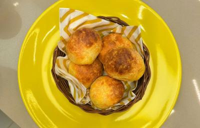 Fotografia em tons de amarelo com um prato amarelo ao centro. Dentro do prato existe uma cestinha com vários pãezinhos feito com queijo e Ninho Adulto