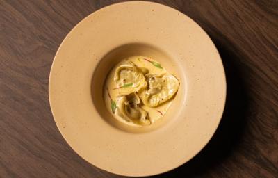 Foto da receita de Ravioli de Escargot feito no Masterchef 11. Observa-se um prato fundo visto de cima com três raviolis servidos com molho e decorado com brotos.