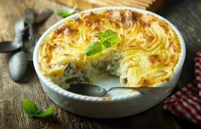 Foto em tons de amarelo da receita de torta de bacalhau servida em uma forma de porcelana branca com uma fatia cortada separada da torta e uma colher prateada dentro