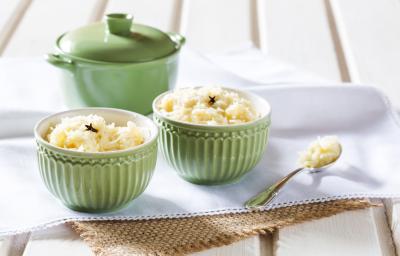 Fotografia de dois potinhos verdes com cocada dentro e uma colher de chá com cocada sobre guardanapos branco e bege, ao lado potinho verde com tampa, tudo sobre uma bancada branca.