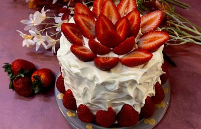 Receita de Bolo Confeitado com Chantininho. Observa-se um bolo alto coberto com chantinho e decorado com morangos.