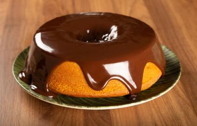 Foto da receita de Bolo de Cenoura. Observa-se o bolo em um prato de porcelana com calda de chocolate por cima escorregando.