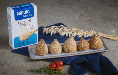 Foto da Receita de Coxinha da Batata Doce com Nestlé Aveia Flocos Finos, servidas em um prato cinza retangular, ao todo são 5, numa bancada de pedra com um tecido azul escuro, uma caixa de nestlé aveia flocos finos.