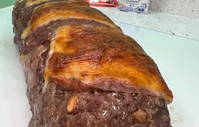 Foto da receita de rocambole de carne moída servida em uma porção grande sobre uma mesa branca