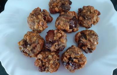 Foto em tons de marrom da receita de cookies de frutas secas e mucilon servida em diversas porções sobre um prato de porcelana branco