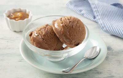 Foto da receita de MOÇA Sorvete de Doce de Leite. Observa-se um potinho individual de vidro com duas bolas de sorvete e, atrás, um potinho com doce de leite cremoso.