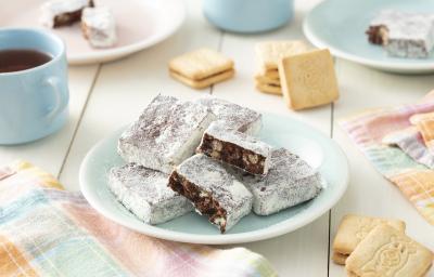 Foto em tons de azul claro da receita de palha italiana de passatempo com leite ninho servida em algumas porções sobre um prato de porcelana azul com biscoitos passatempo em volta além de uma xícara de café azul e um paninho quadriculado para decorar