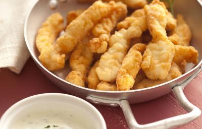 Fotografia em tons de vinho, branco e dourado, abaixo potinho branco com molho de iogurte, acima caçarola de inox contendo peixe empanado e frito decorado com ramo de salsa, ao lado guardanapo branco, tudo sobre bancada na cor vinho.