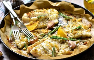 Fotografia de quatro filés de peixe assados com MAGGI MEU SEGREDO 7 Vegetais, ervas frescas e amêndoas. O assado está sobre papel manteiga e dentro de uma forma preta.