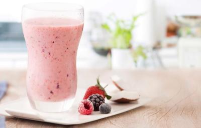 fotografia e tons de rosa e branco de uma bancada bege vista de frente, contém um copo transparente com a bebida de frutas vermelhas e ao lado contém frutas vermelhas.