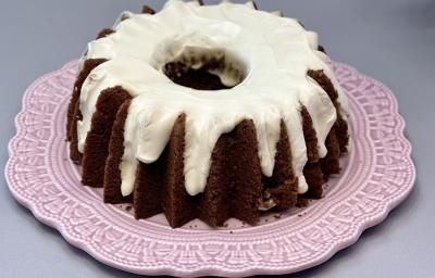 Foto da receita de bolo de cenoura carrot cake servida em uma porção inteira sobre um prato de porcelana cor de rosa em cima de uma mesa cinza