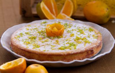 Foto aproximada da receita de bolo de casca de laranja, servido em um prato e decorado com açúcar e raspas de laranja.