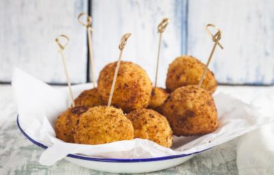 fotografia em tons de branco e bege de uma bancada cinza vista de frente. Contém um prato redondo branco com bolinhos de arroz frito, e por cima palitos.