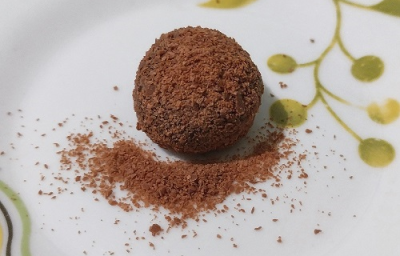 Foto da receita de Brigadeiro de Café. Observa-se um brigadeiro em um prato branco decorado com o café polvilhado por cima.