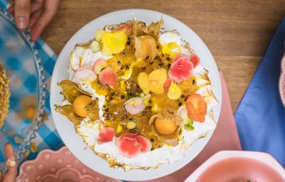 Foto vista de cima do Bolo de Frutas Amarelas, decorado com flores comestíveis, polpa de maracujá e pedaços de manga