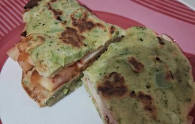 Fotografia de uma panqueca de brócolis recheada com tomate e peito de peru, cortada na metade, sobre um prato branco com borda vermelha.