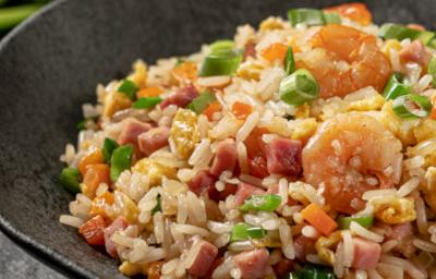 Foto aproximada de um prato preto fundo com a receita de arroz chop suey dentro, decorado com cebolinhas e com camarões e presuntos em cubos.