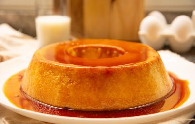 Fotografia mostra uma torta com textura delicada e cremosa, coberta por uma calda de caramelo dourada e servida em um prato branco.