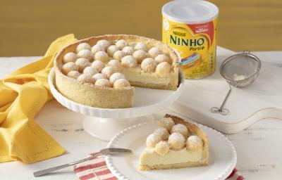 Fotografia em tons de branco e laranja de um prato redondo laranja com uma torta com recheio branco e brigadeiros brancos enrolados.