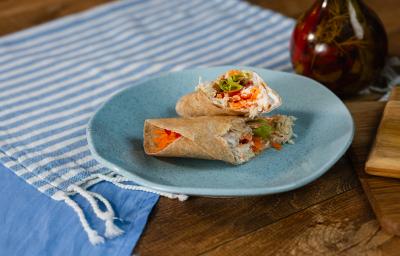 Fotografia em tons de azul com um prato azul ao centro. Em cima do prato existe uma receite de wrap recheada com frango desfiado, creme de ricota, tomate e alface.