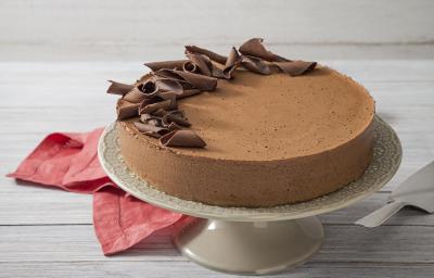 Fotografia em tons de branco e vermelho de uma bancada de madeira branca com um paninho vermelho, sobre ele uma bailarina branca com a torta mousse de chocolate decorada com raspas de chocolate.