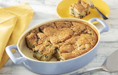 Foto da receita de Torta de Legumes de Liquidificador. Observa-se um refratário oval branco com a torta assada dentro, cortada em fatias quadradas. Atrás, um pratinho amarelo com uma fatia da torta.