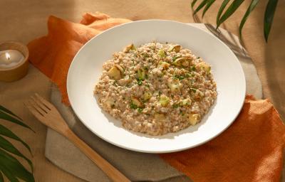 Foto da receita de risoto de abobrinha vegano servida em um prato de cerâmica com um garfo de madeira ao lado sobre um paninho laranja