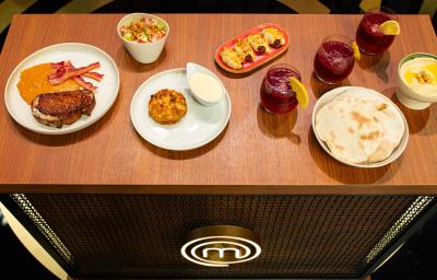 Fotografia de uma mesa de madeira com um brunch com pão sírio, hommus, ovos, frutas, massa folhada, creme inglês de requeijão, crumble de banana e torrada. Todas as partes estão porcionadas em recipientes brancos e separados.