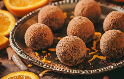 Fotografia mostra Pequenas bolinhas de trufa de chocolate cobertas por uma camada generosa de cacau em pó, ao lado rodelas de laranja.