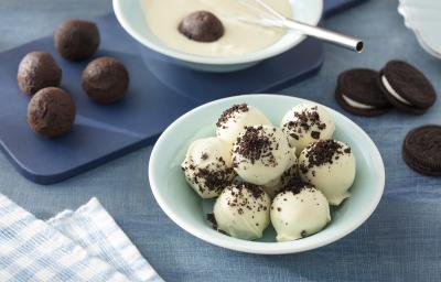 Foto da receita de Trufa de Negresco. Observa-se um recipiente verde menta com as tufas dentro cobertas de chocolate branco. Atrás, uma tábua azul com as trufas sem cobertura e a foto está decorada com biscoitos Negresco.