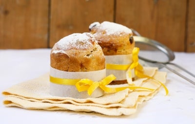 Fotografia mostra um mini panetone em forminha branca, com um laço amarelo em volta. Fotografia mostra um mini panetone em forminha branca, com um laço amarelo em volta.