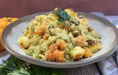 Foto da receita de Cuscuz Marroquino. Observa-se um prato de cerâmica claro redondo contendo a receita finalizada com um ramo de salsa verde.