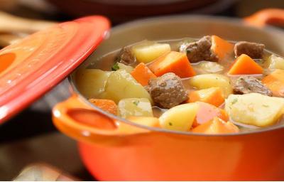 foto tirada de uma panela laranja com pedaços de carne com colorau, batata e abóbora e ao lado a tampa