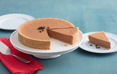 fotografia em tons azul e branco. Contém três pratos brancos, um deles esta com uma fatia de torta e o outro com a torta para servir. Ao lado um pano vermelho com uma espátula por cima. O terceiro prato esta vazio.