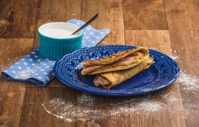 Imagem em tons de marrom e azul claro e escuro. No centro há um prato azul com duas quesadillas recheadas e, ao lado esquerdo, há um tecido azul com bolinhas brancas e, sobre ele, um pote azul com o creme azedo e uma colher.