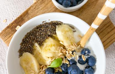 Foto da receita de bowl plant-based. Observa-se um bowl branco com mirtilos, banana, aveia e chia sobre uma tábua de madeira.