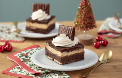 Foto da receita de Mini Ópera Cake, em um prato branco, sobre uma bancada de madeira decorada com itens natalinos e uma colher dourada