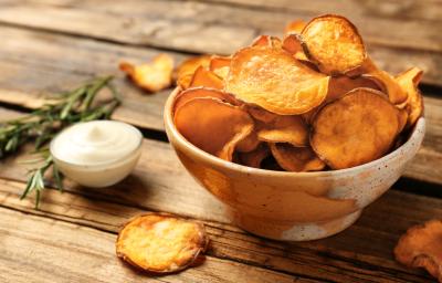 Fotografia em tons de marrom com um prato fundo de cerâmica ao centro. Em cima do prato existe uma porção de chips de batata doce feitos na Air Fryer