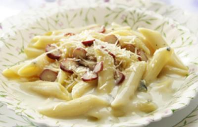 Fotografia tirada de uma prato redondo branco com macarrão e creme branco e pedaços de pinhões