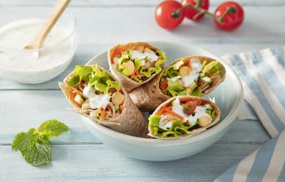 Foto em tons coloridos da receita de wrap vegetariano com molho de hortelã servida em 4 porções dentro de um bowl de porcelana branca sobre uma mesa de madeira azul clara com um paninho listrado azul e um pote de iogurte natural