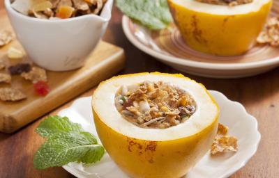 Fotografia em tons de amarelo em uma bancada de madeira, pratos brancos, bege e tábua de madeira cada um com um maracujá doce aberto recheado com Nesfti Cereal Matina com frutas.